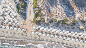 Vista aérea de una playa con hileras de sombrillas y un camino de madera.