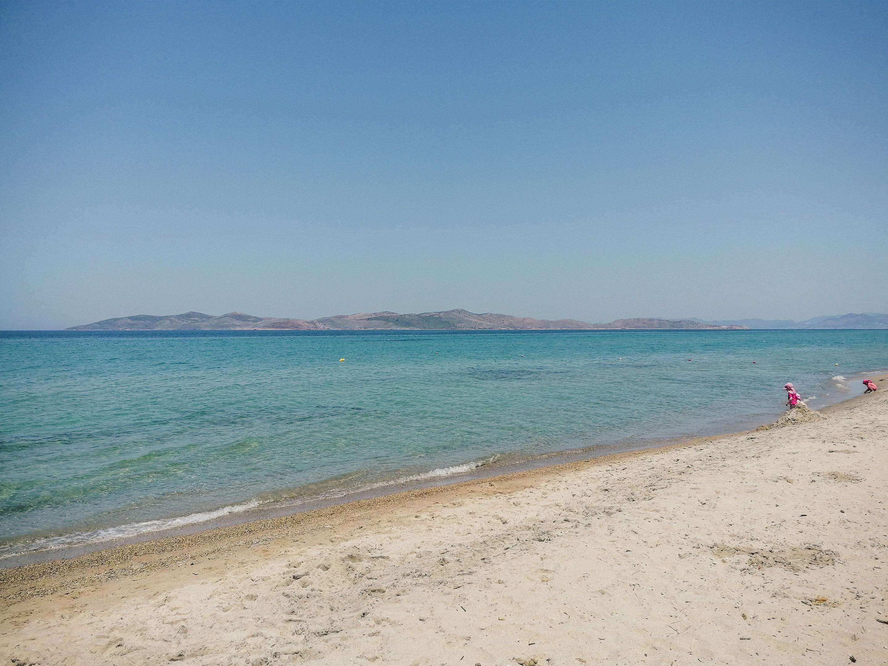 Una playa con agua cristalina y montañas a lo lejos.
