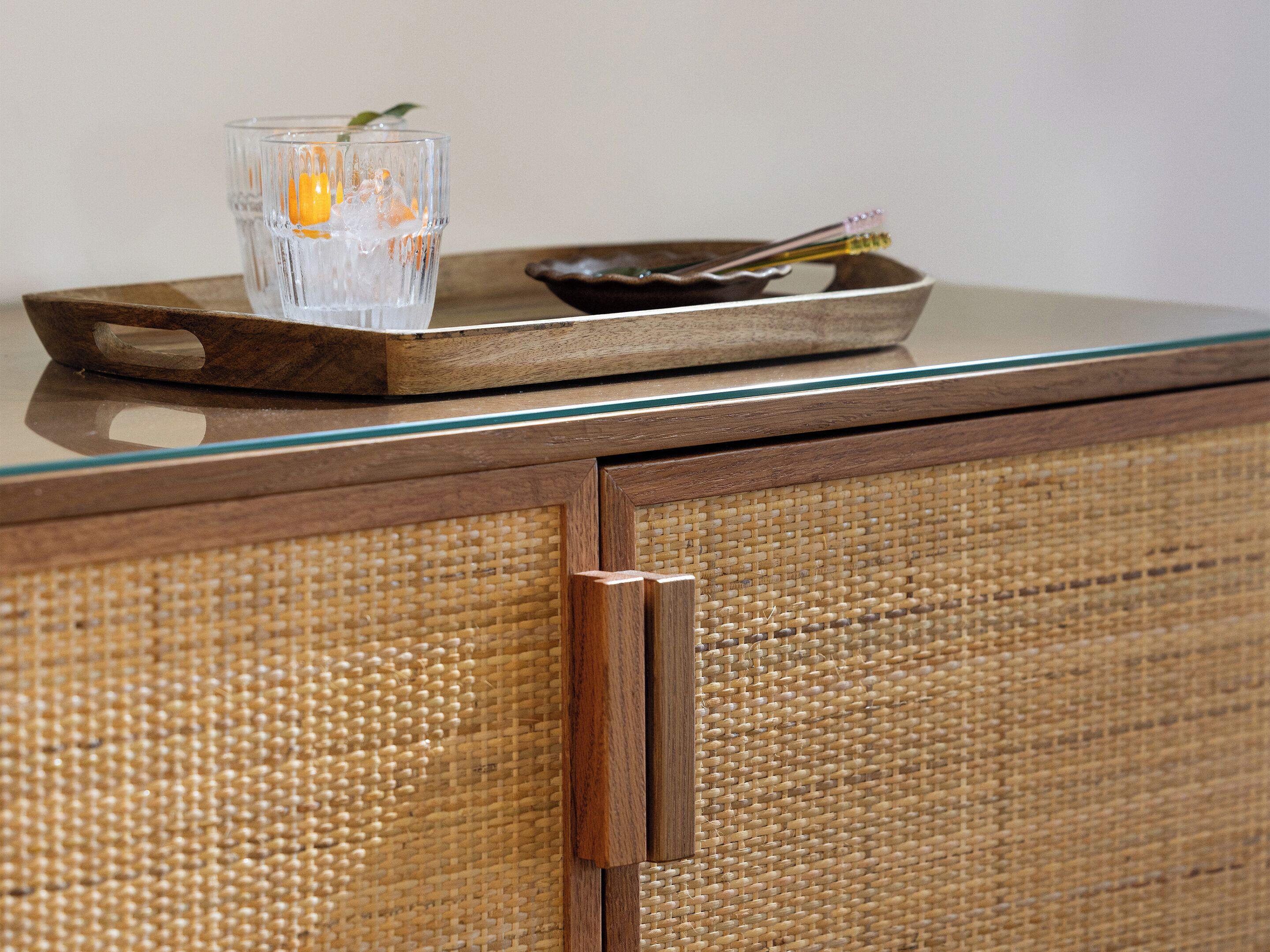 Una bandeja de vidrio con una vela y una cuchara sobre un mueble de madera con un panel trasero tejido.