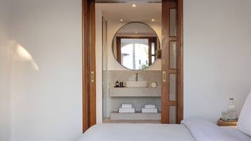 A bedroom with a bed, a wooden door leading to a bathroom with a sink and mirror.