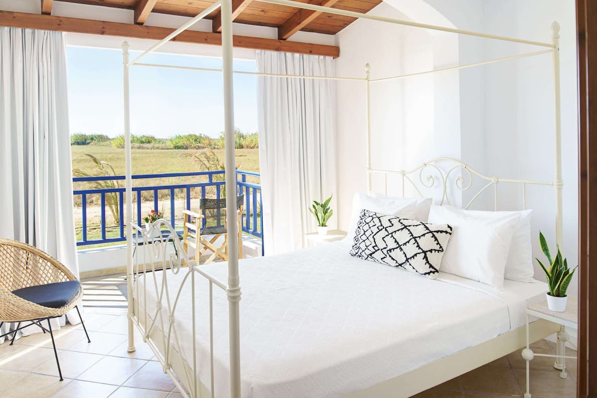 A bedroom with a four-poster bed, a balcony with a blue railing, and a view of the countryside.