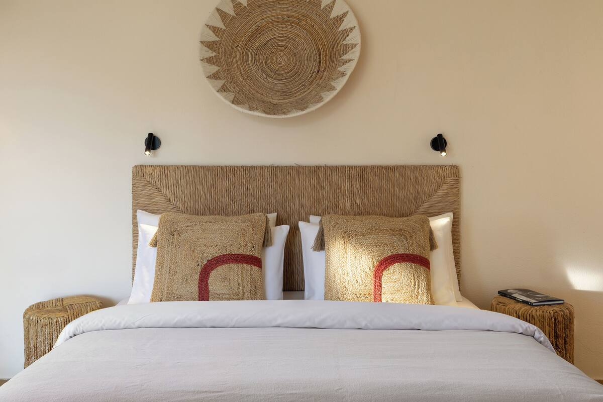 A bed with a woven headboard, two bedside tables, and a wall-mounted decorative piece.