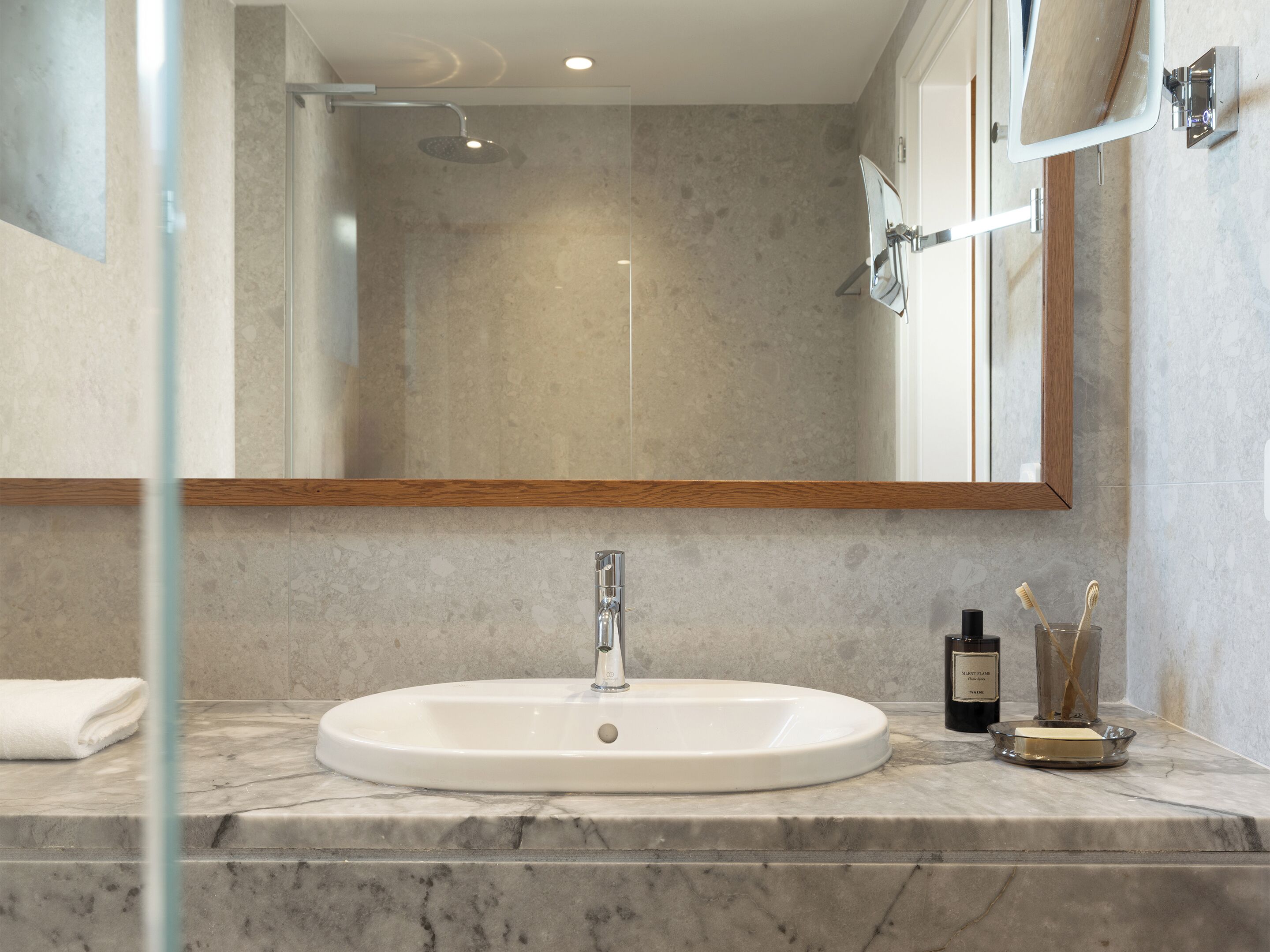 Une salle de bain avec un lavabo blanc, une douchette à main, un miroir et une serviette posée sur le comptoir.