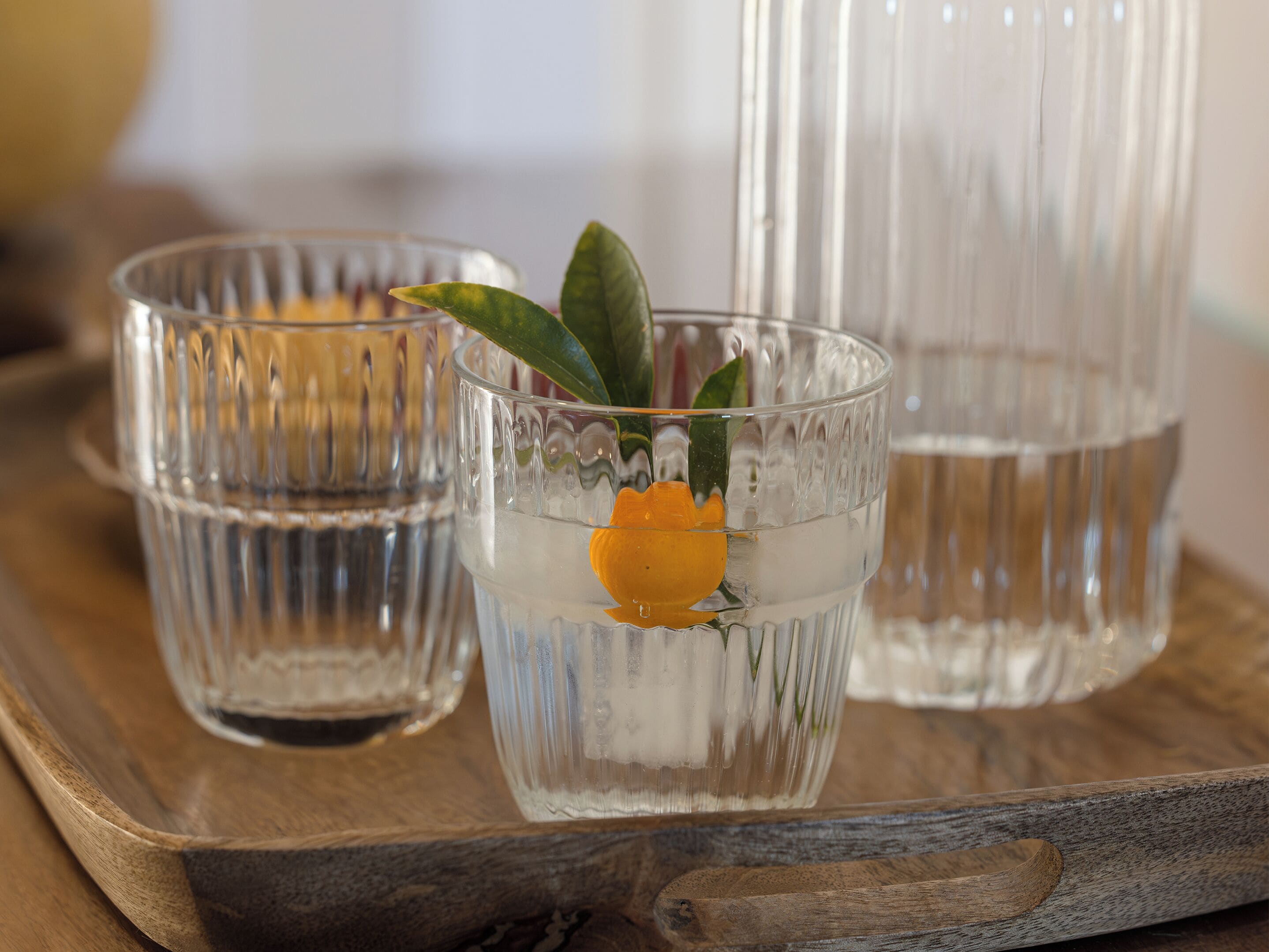 Three glass containers with water and a lemon slice on a wooden tray.