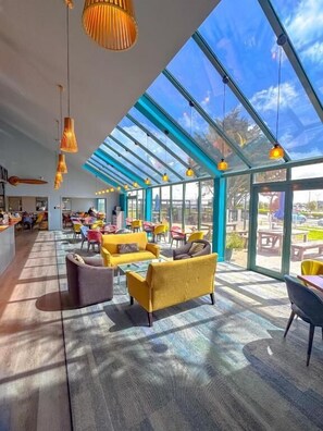 A spacious indoor area with a high ceiling, large windows, and modern furniture. - JetPark Hotel Hamilton Airport (Ohaupo)