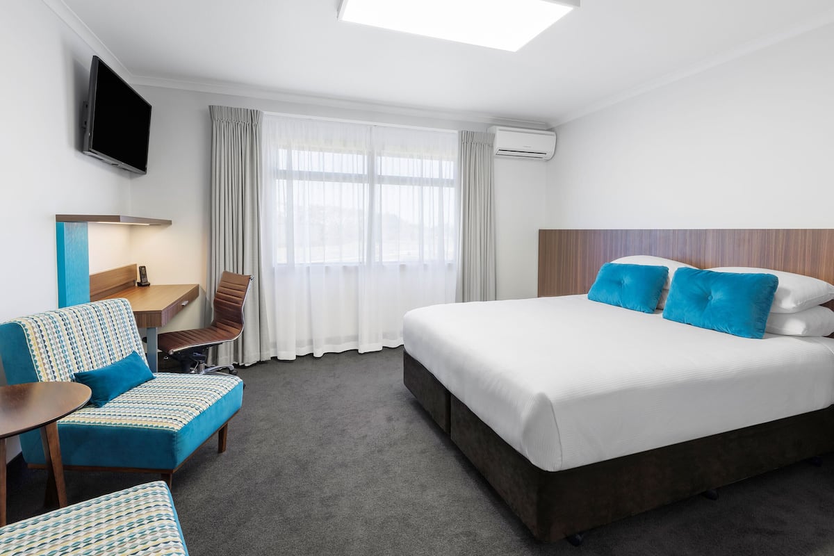 A hotel room with a large bed, a desk with a chair, a sofa, and a TV mounted on the wall.
