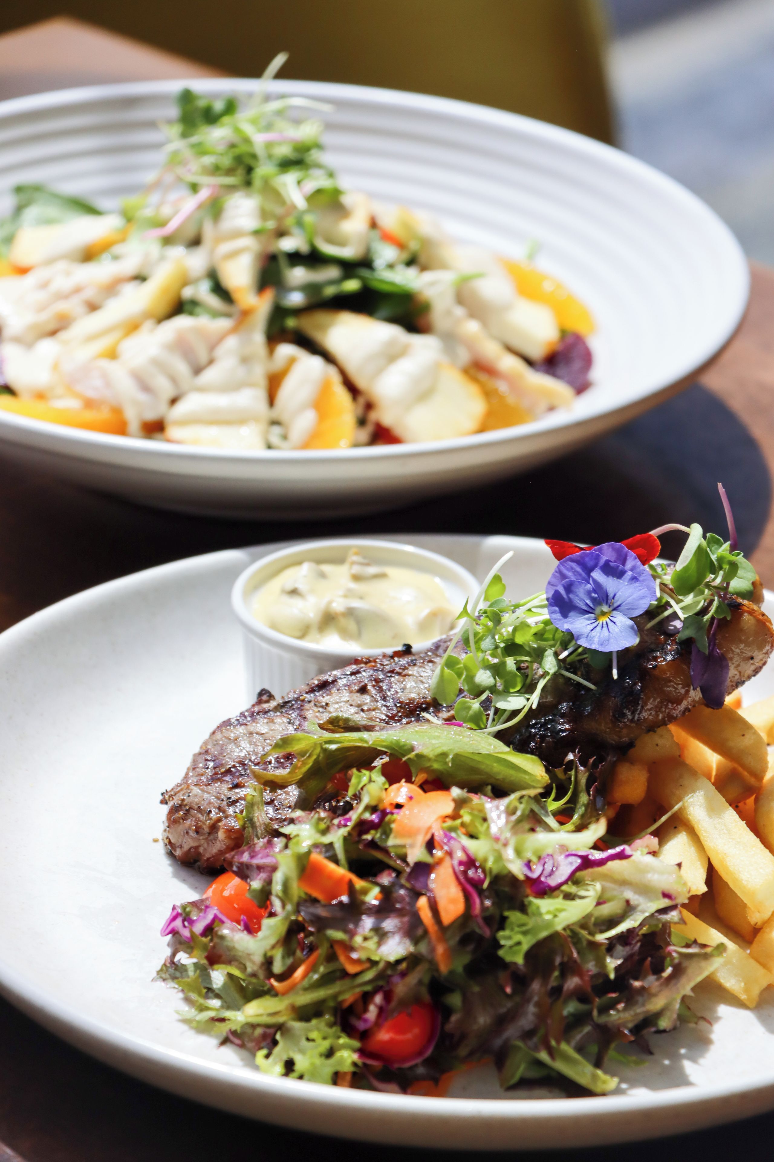 Uma mesa de jantar com dois pratos de comida: um com bife e legumes, e outro com salada e batatas fritas.