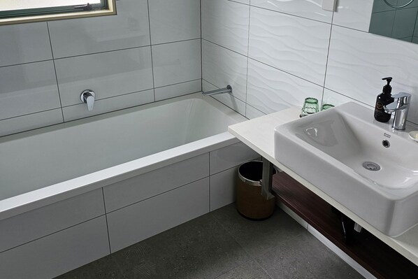 A modern bathroom with a white bathtub, a sink, and a trash can.