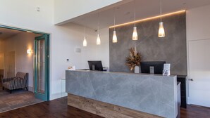A reception desk with a modern design, featuring a grey marble top and wooden base. There are three pendant lights hanging above the desk.