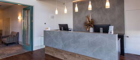 A reception desk with a modern design, featuring a grey marble top and wooden base. There are three pendant lights hanging above the desk.