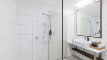 Ett modernt badrum med en dusch som är avskärmad med glasväggar, ett vitt handfat och en stor spegel.