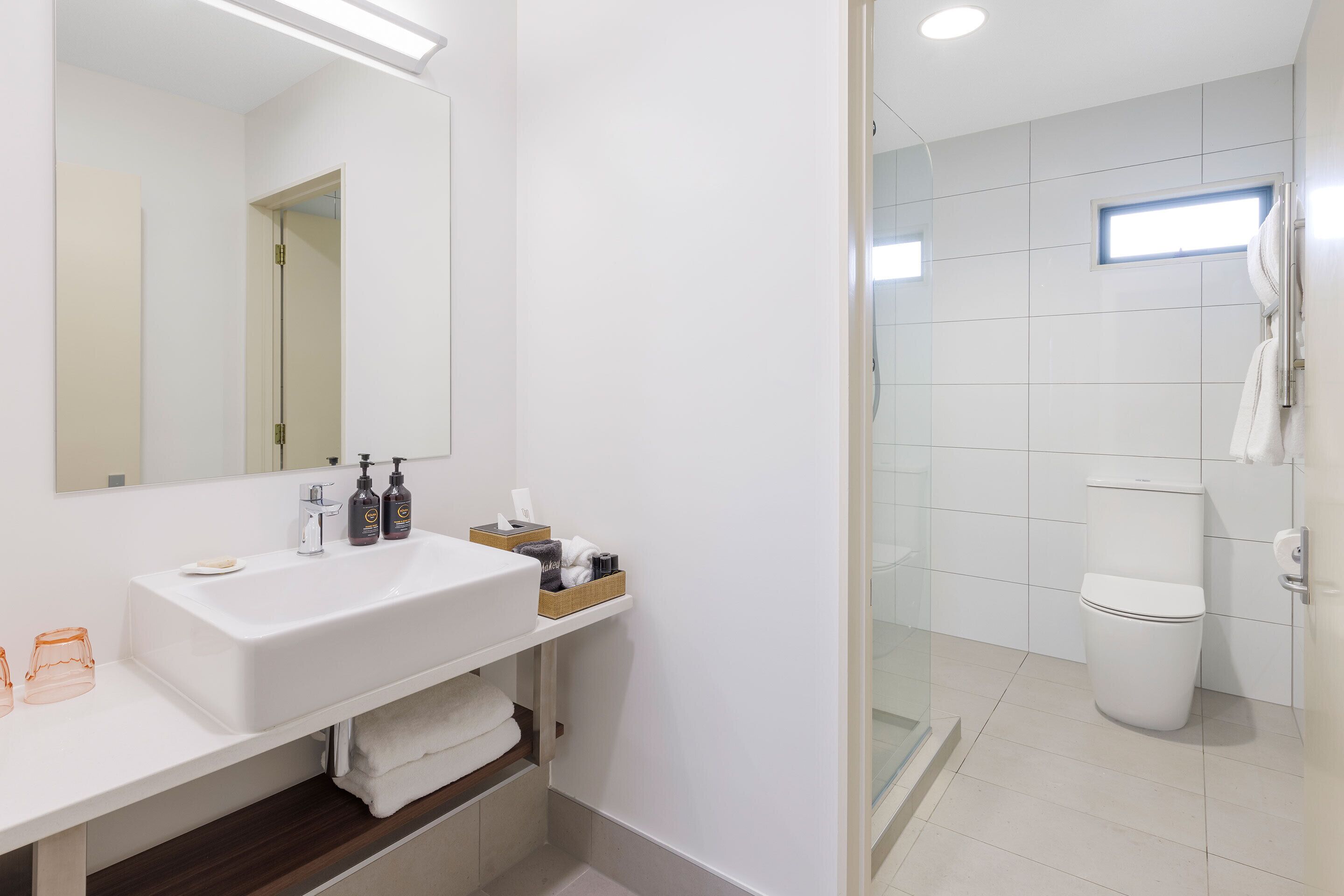A modern bathroom with a white sink, mirror, and glass shower enclosure.