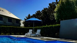 A swimming pool with clear blue water, a lounge area with chairs, and a building in the background.