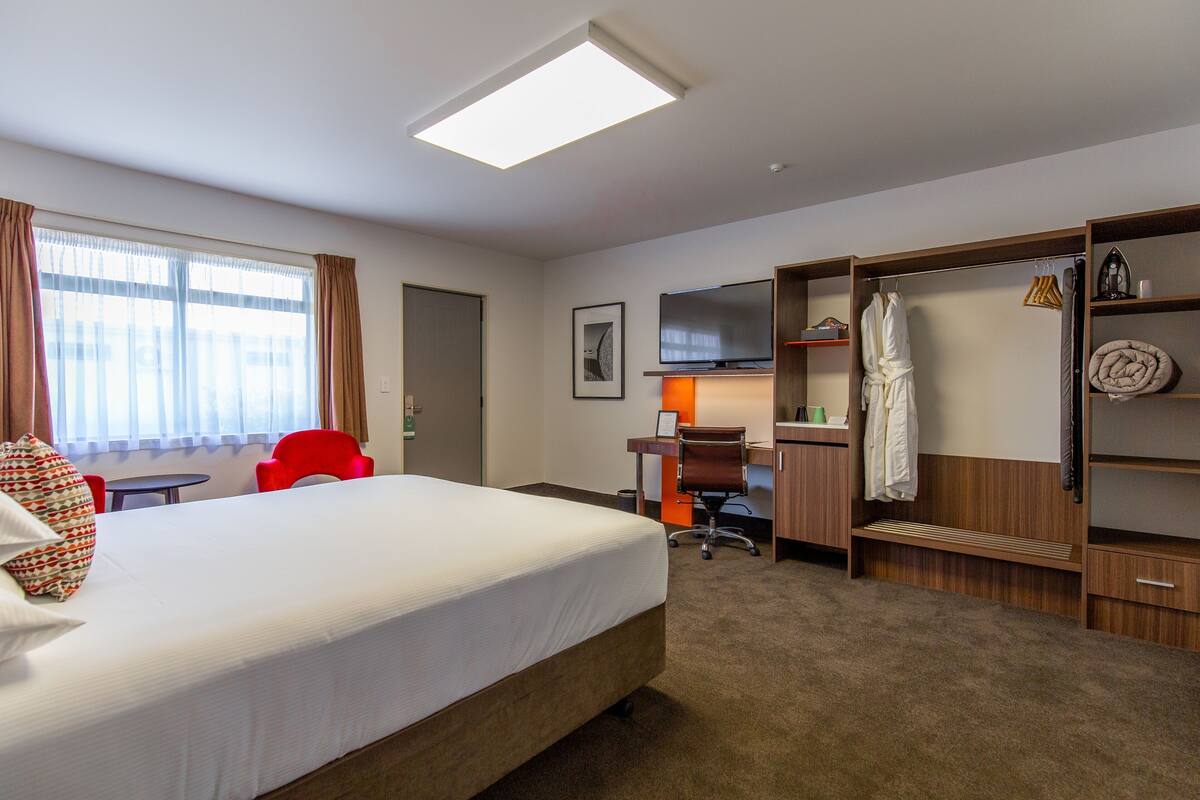 A hotel room with a bed, a desk, a chair, a TV, a wardrobe, and a window with curtains.