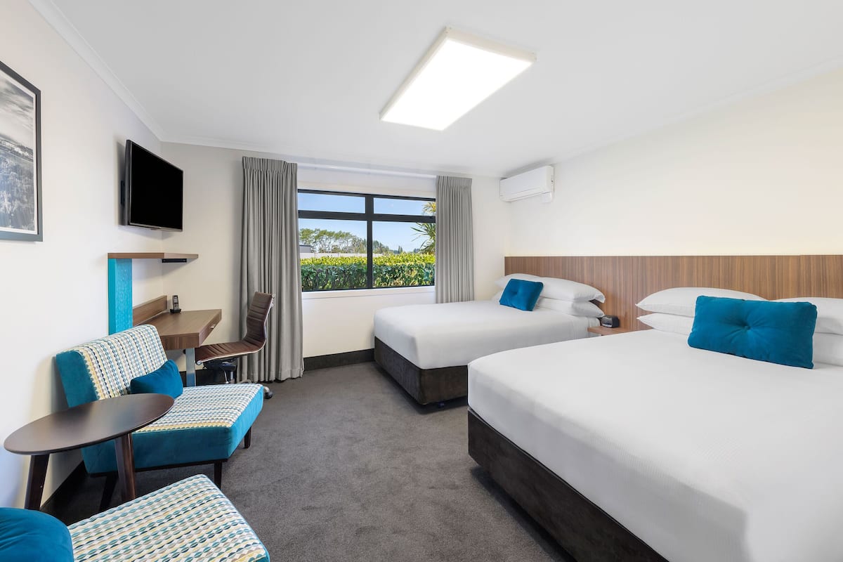 A hotel room with two beds, a TV, a small table, and a seating area.