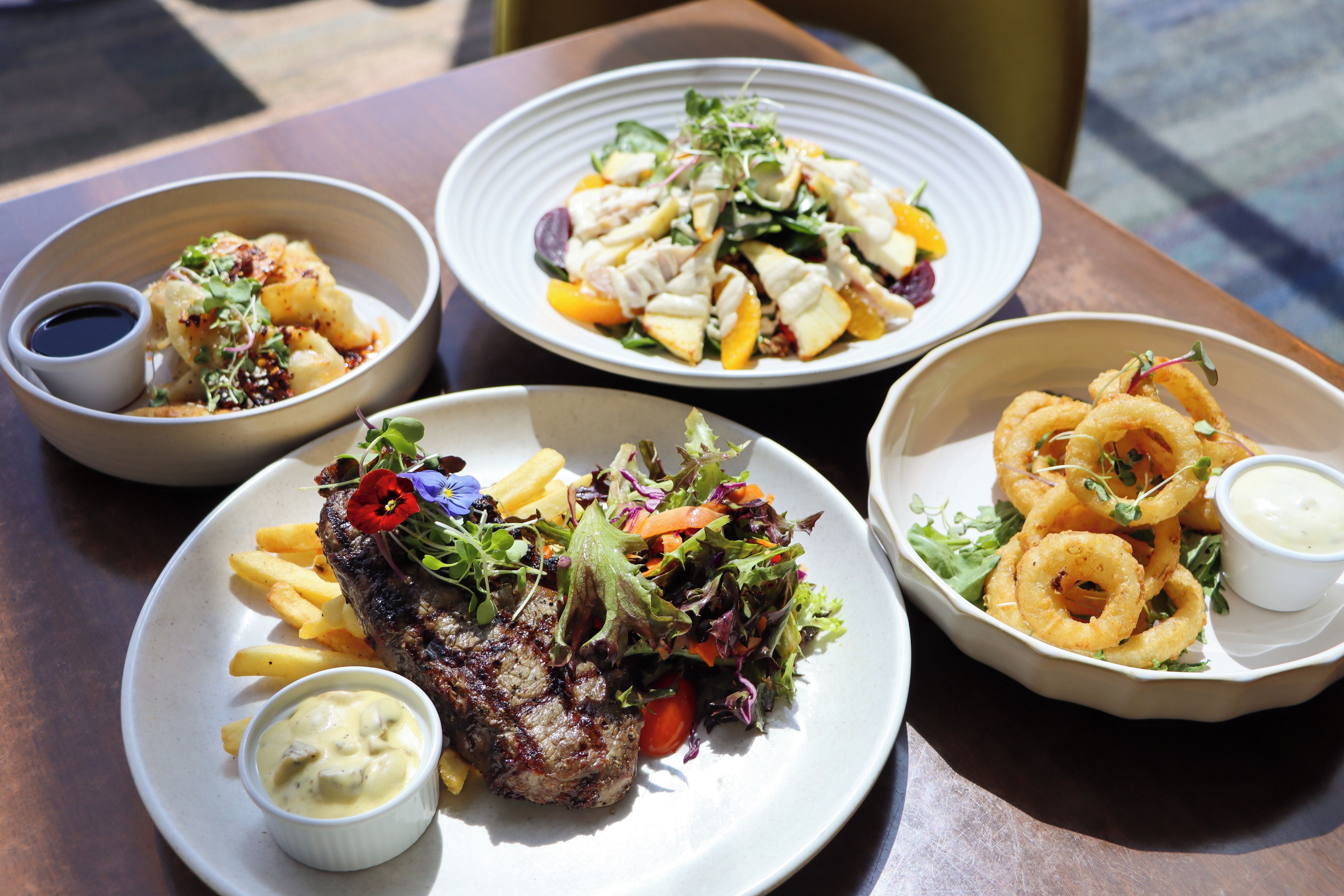 Ett bord med tre tallrikar mat, inklusive en biff, pommes frites, sallad och lökringar.