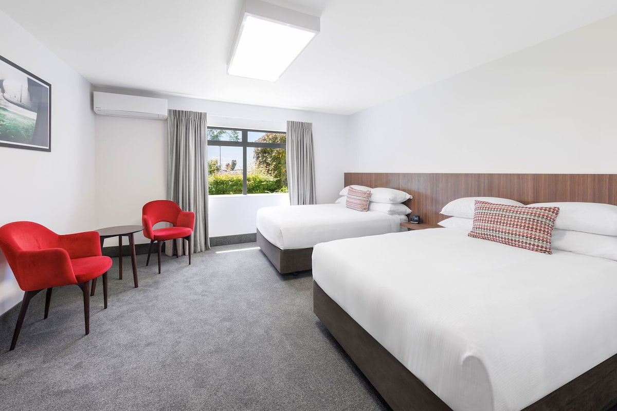 A hotel room with two beds, a desk, and chairs.