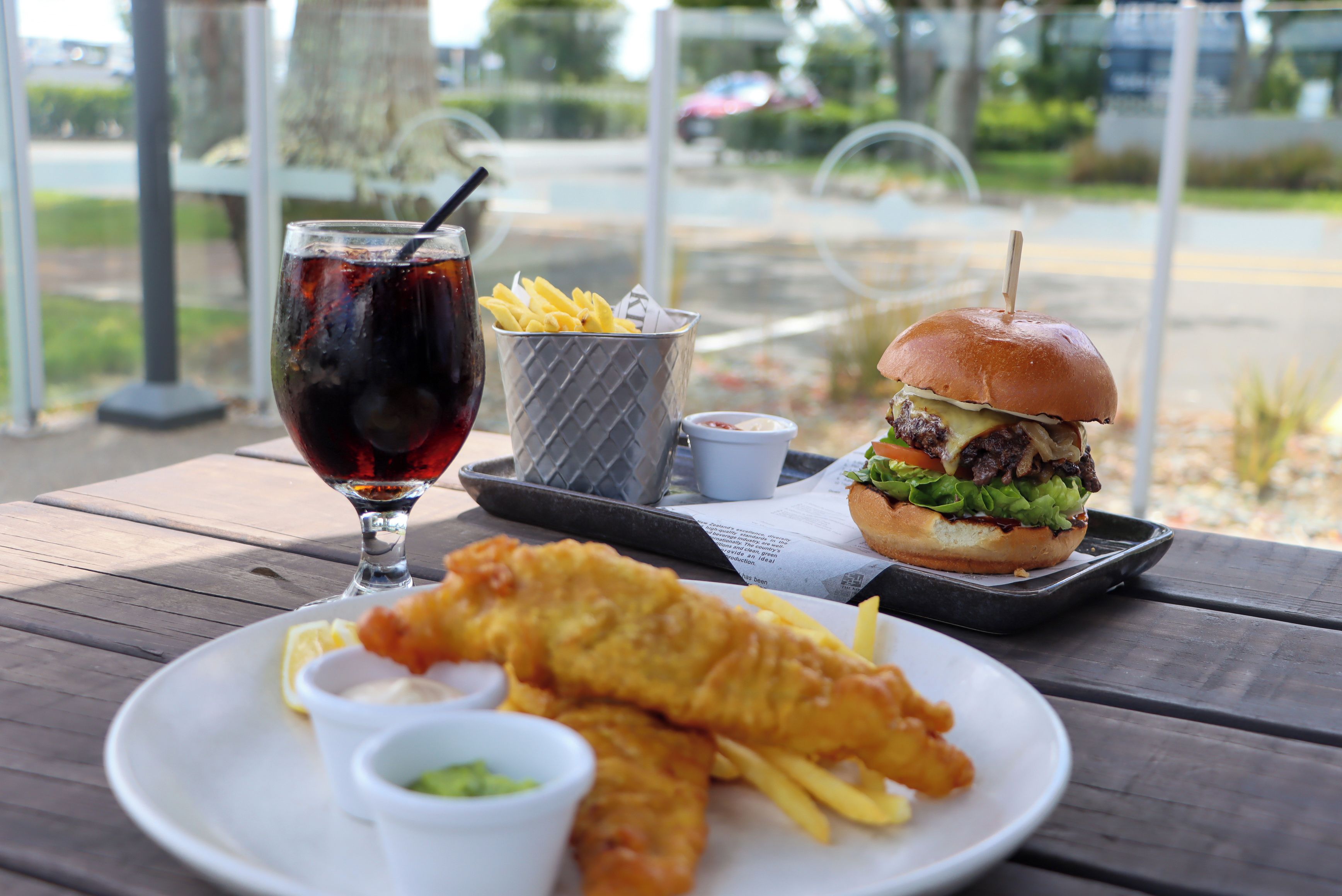 A meal consisting of fish and chips, a burger, and a drink on a wooden table.
