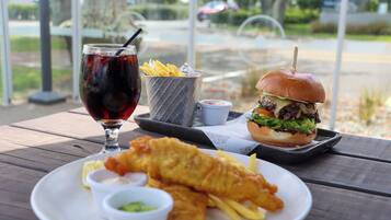 A meal consisting of fish and chips, a burger, and a drink on a wooden table.