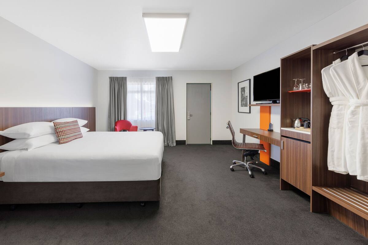 A hotel room with a bed, a desk, a chair, a TV, a wardrobe, and a door.