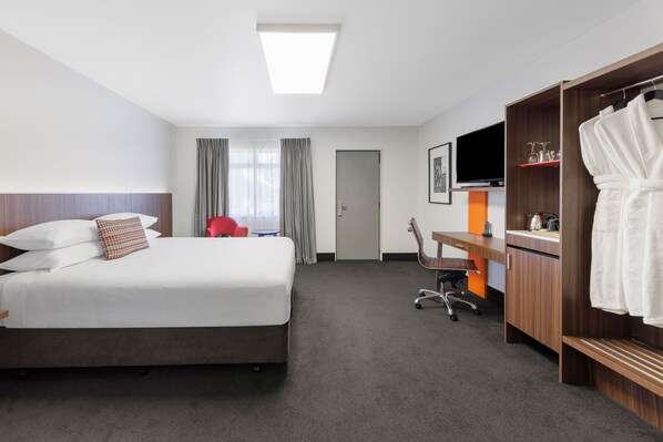 A hotel room with a bed, a desk, a chair, a TV, a wardrobe, and a door.