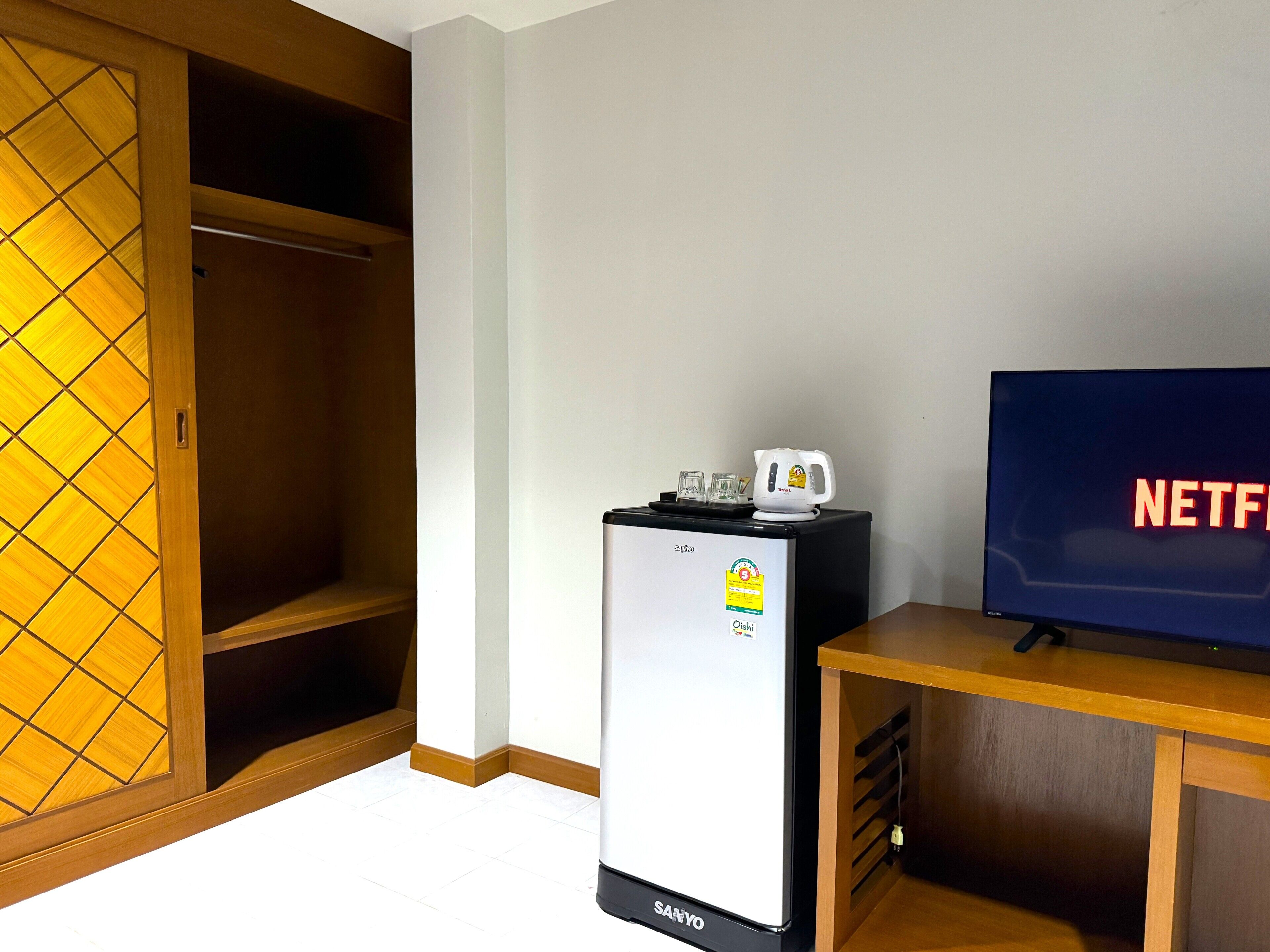A room with a refrigerator, a television displaying the Netflix logo, and a wooden cabinet.