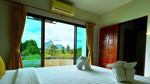 Ein Hotelzimmer mit einem großen Bett, Blick auf eine gebirgige Landschaft durch das Fenster und einer Holztür.