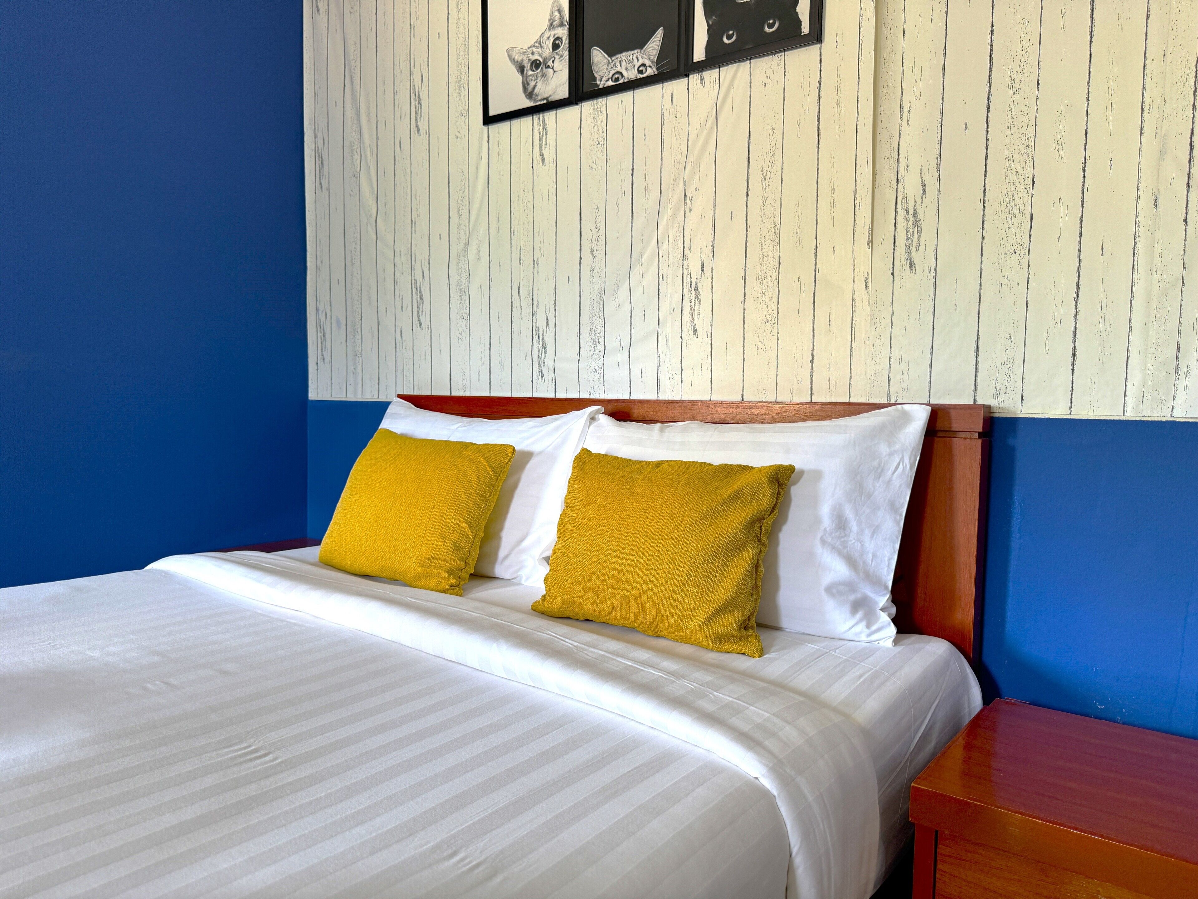 Un lit avec une literie blanche et deux oreillers de couleur jaune moutarde, une tête de lit en bois et un mur orné d’un panneau en bois blanc.