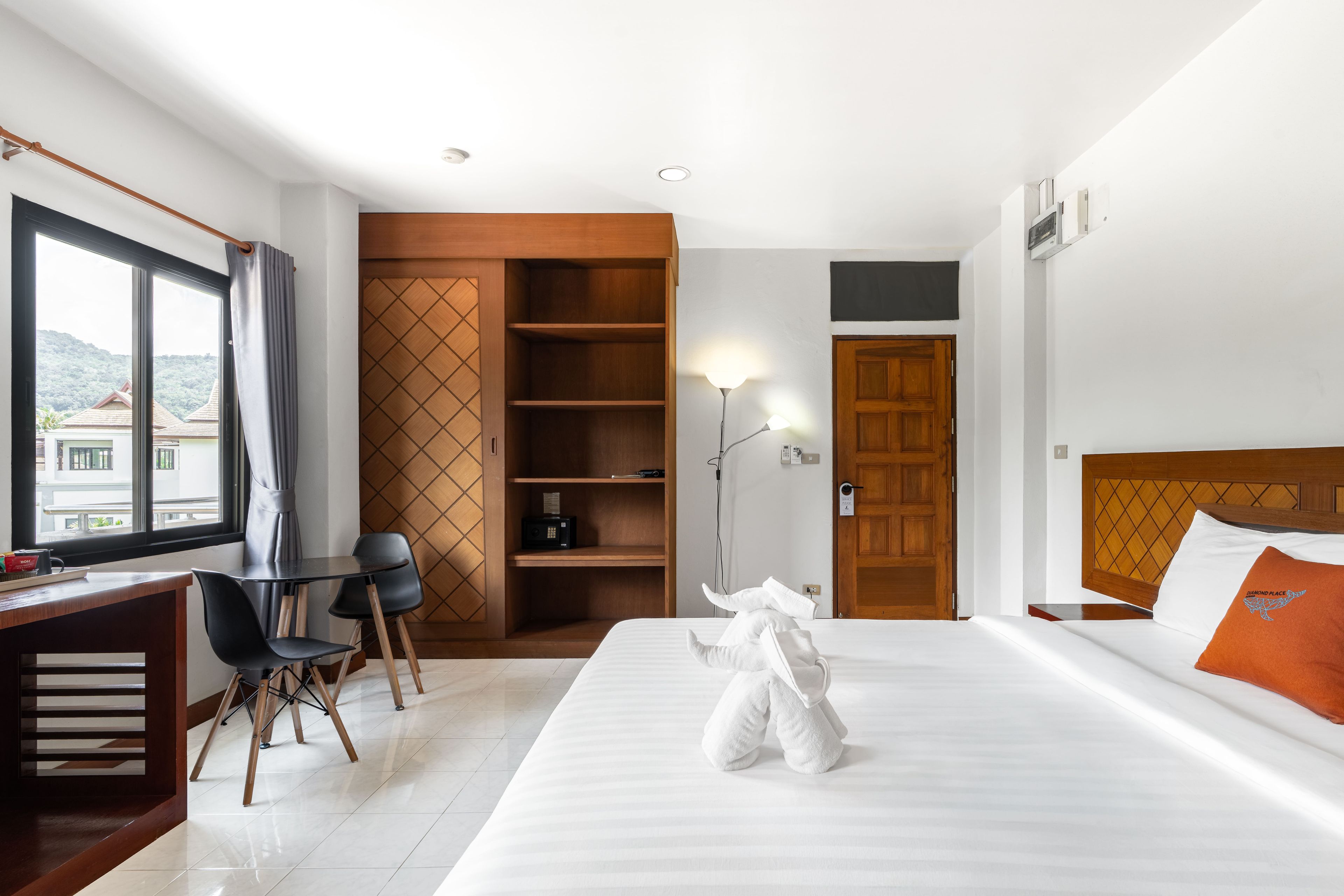 A hotel room with a bed, a desk with chairs, a wardrobe, and a view of the outside.