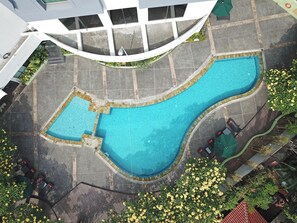 A large, irregularly shaped swimming pool with a tiled border, surrounded by a paved area with a few outdoor tables and chairs. - Cityloog Hotel Tebet Jakarta (Jakarta)
