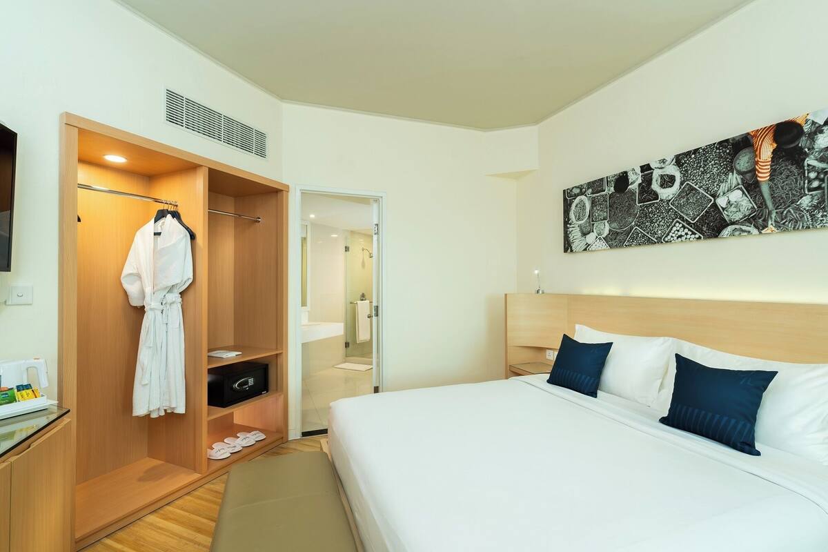 A hotel room with a bed, a wardrobe, a bathroom, and a large abstract painting on the wall.
