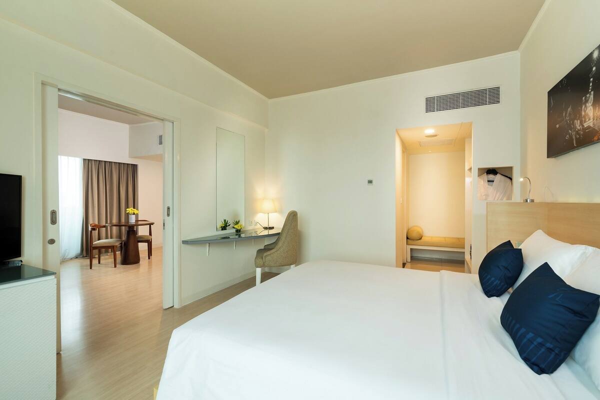 A hotel room with a large bed, a desk with a chair, a television, and a bathroom visible through an open door.