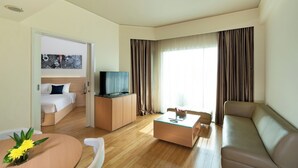 A modern hotel room with a bed, a TV on a wooden cabinet, a sofa, a coffee table, and a dining table with flowers. - Cityloog Hotel Tebet Jakarta (Jakarta)