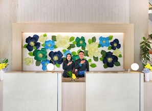 A reception desk with a floral wall mural, two receptionists, and a small plant on the counter. - Cityloog Hotel Tebet Jakarta (Jakarta)