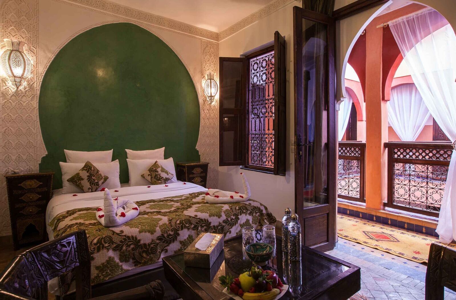 Habitación de hotel con una cama grande, un balcón con vistas y una zona de comedor con frutero.