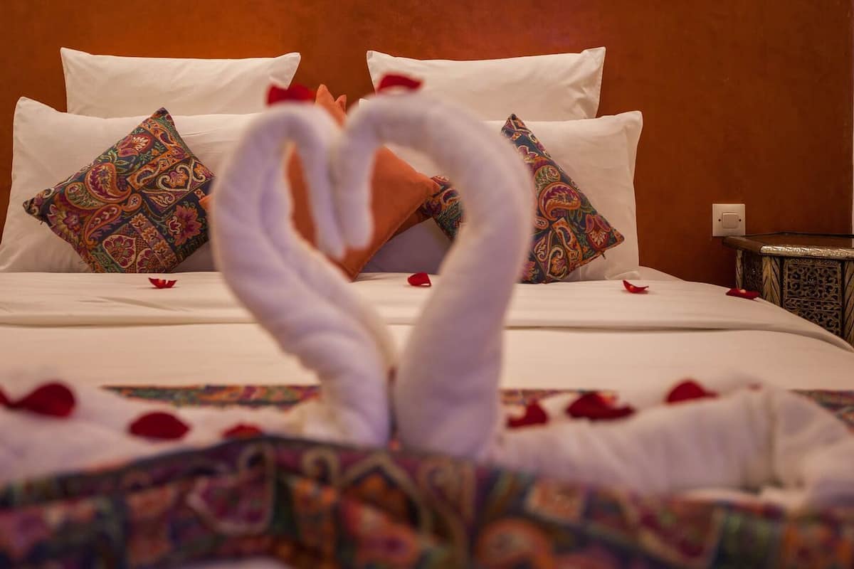 A bed with white linens, a heart-shaped towel arrangement, and decorative pillows.