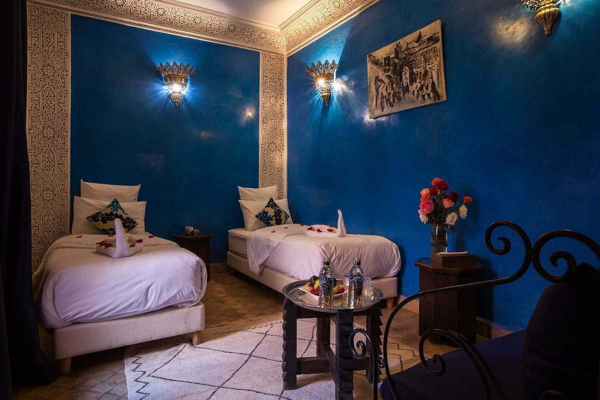 A room with two beds, a small table with drinks, and a wall with a painting.