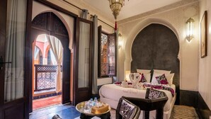 A hotel room with a bed, a chair, a small table with water bottles, and a decorative wall lamp. - Riad Alaka (Marrakech)