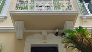 A building with a balcony, a door with a decorative metal grille, and a window with green shutters. - Rent Cannes Meublés Gambetta (Cannes)