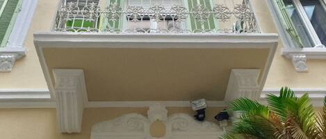Un immeuble doté d’un balcon, d’une porte ornée d’une grille en métal décorative et d’une fenêtre avec des volets verts.