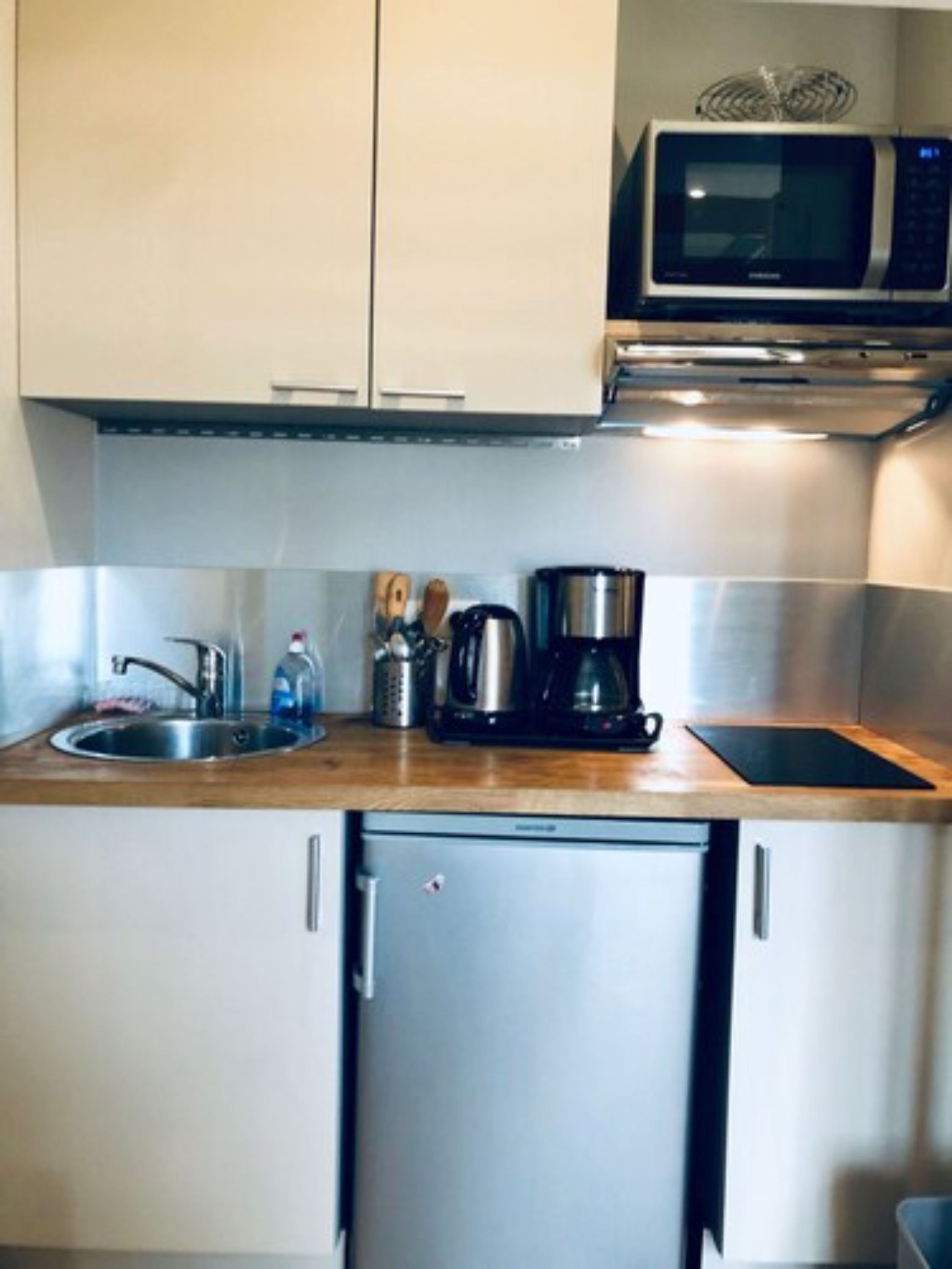A compact kitchen with a stainless steel refrigerator, a microwave, a coffee maker, and a sink.
