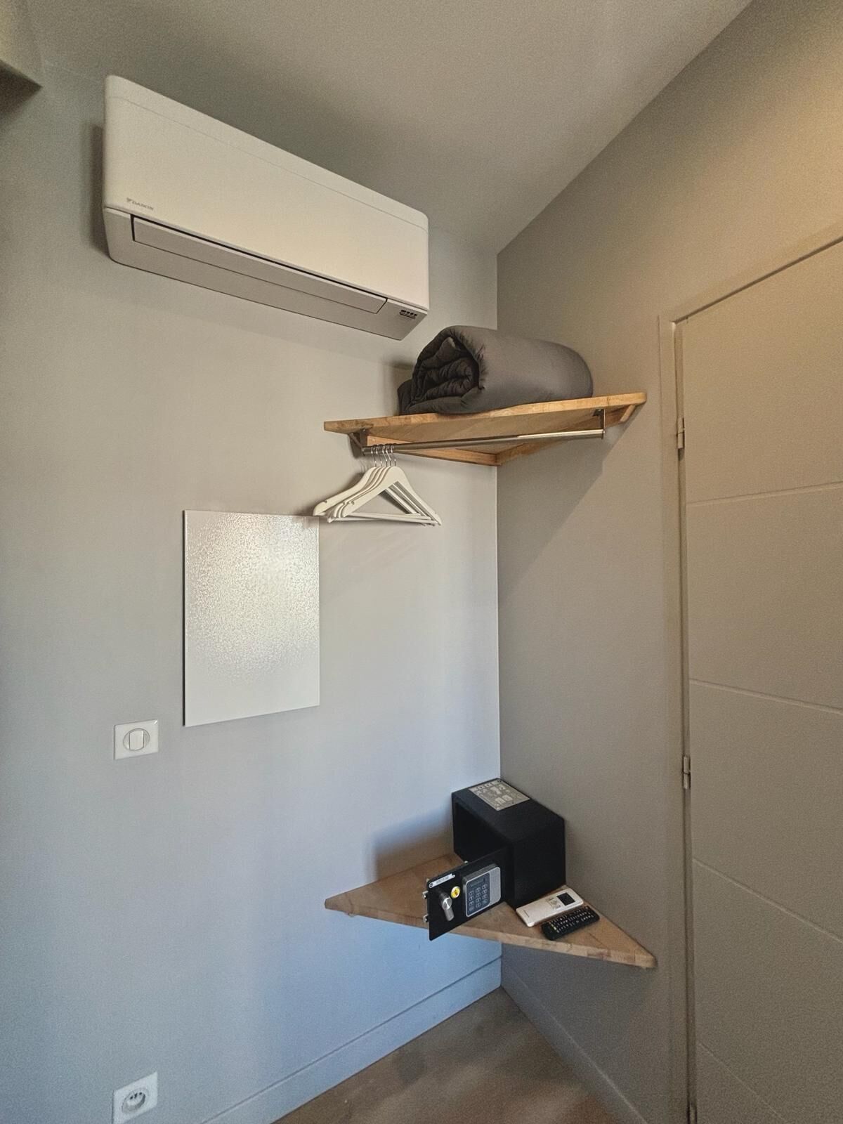 A compact bathroom with a built-in air conditioner, a towel rack, a small shelf with a remote control, and a wall-mounted light switch.