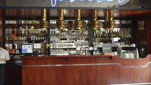 Un coin bar agrémenté d’un néon indiquant « cafésilver », d’étagères remplies de bouteilles et de verres, et d’un écran d’ordinateur posé sur le comptoir.