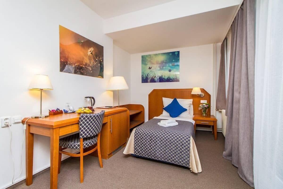 Habitación de hotel con cama, escritorio, silla, mesita de noche y dos lámparas de pared.