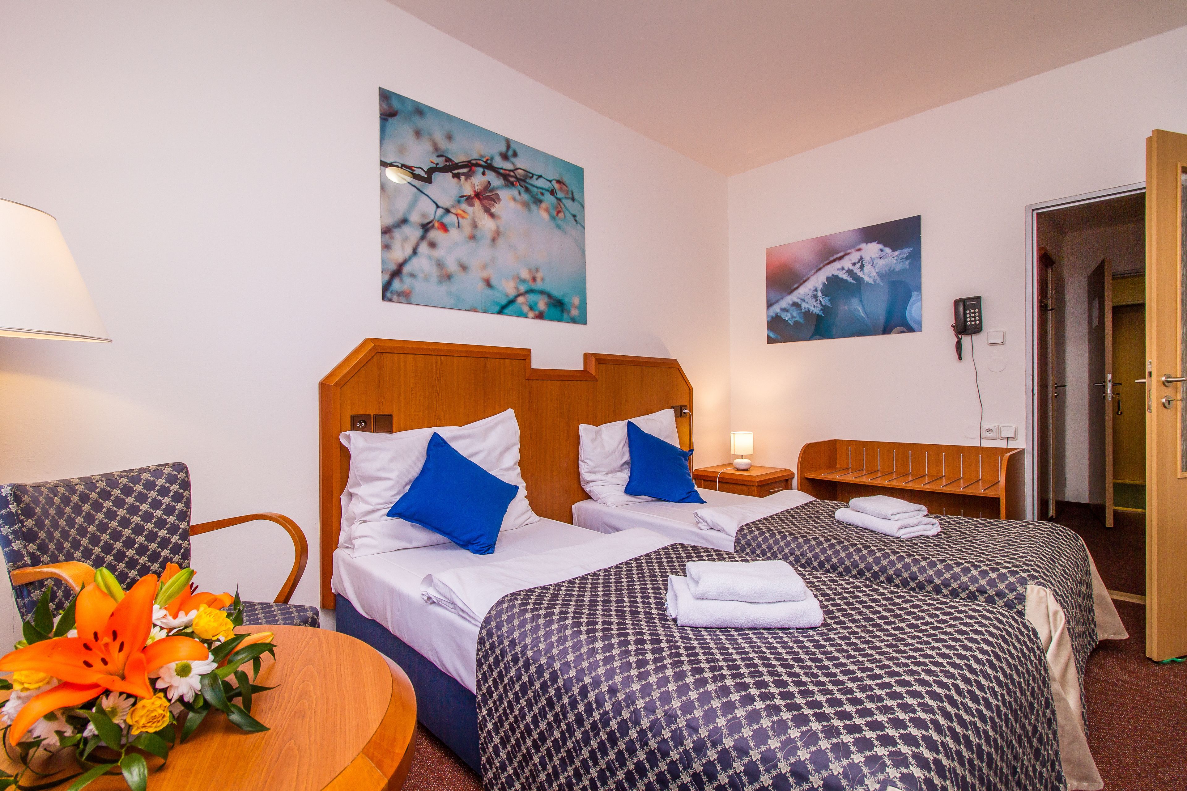 A hotel room with two beds, a wooden headboard, a desk with a lamp, and a chair.