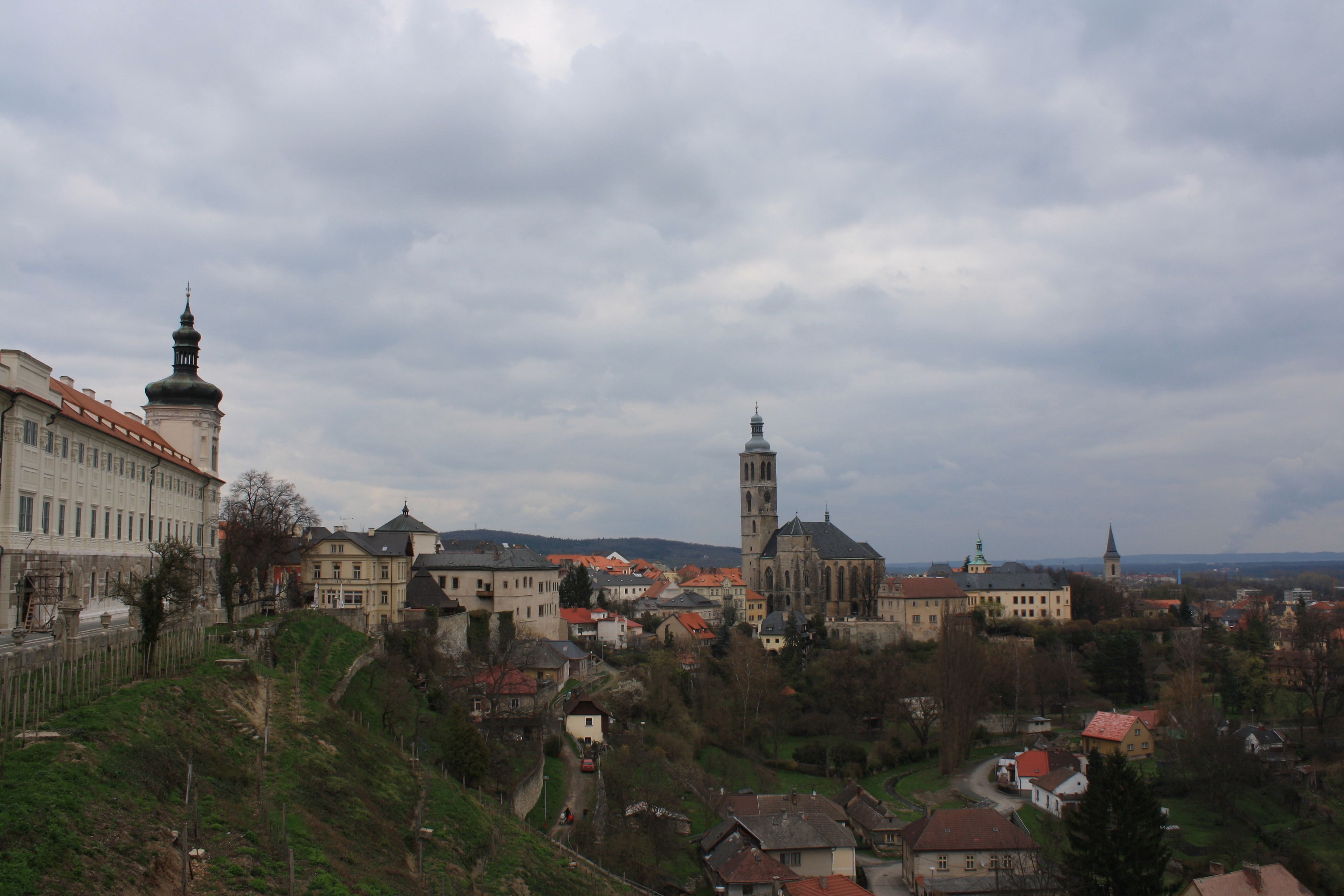 A historic town with a prominent church featuring a tall bell tower, surrounded by residential buildings and a hilly landscape.