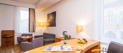 A hotel room with a wooden desk, two armchairs, a sofa, a small table, and a lamp.