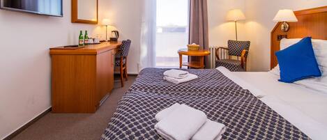 A hotel room with a bed, a desk, a chair, a television, and a window with curtains.