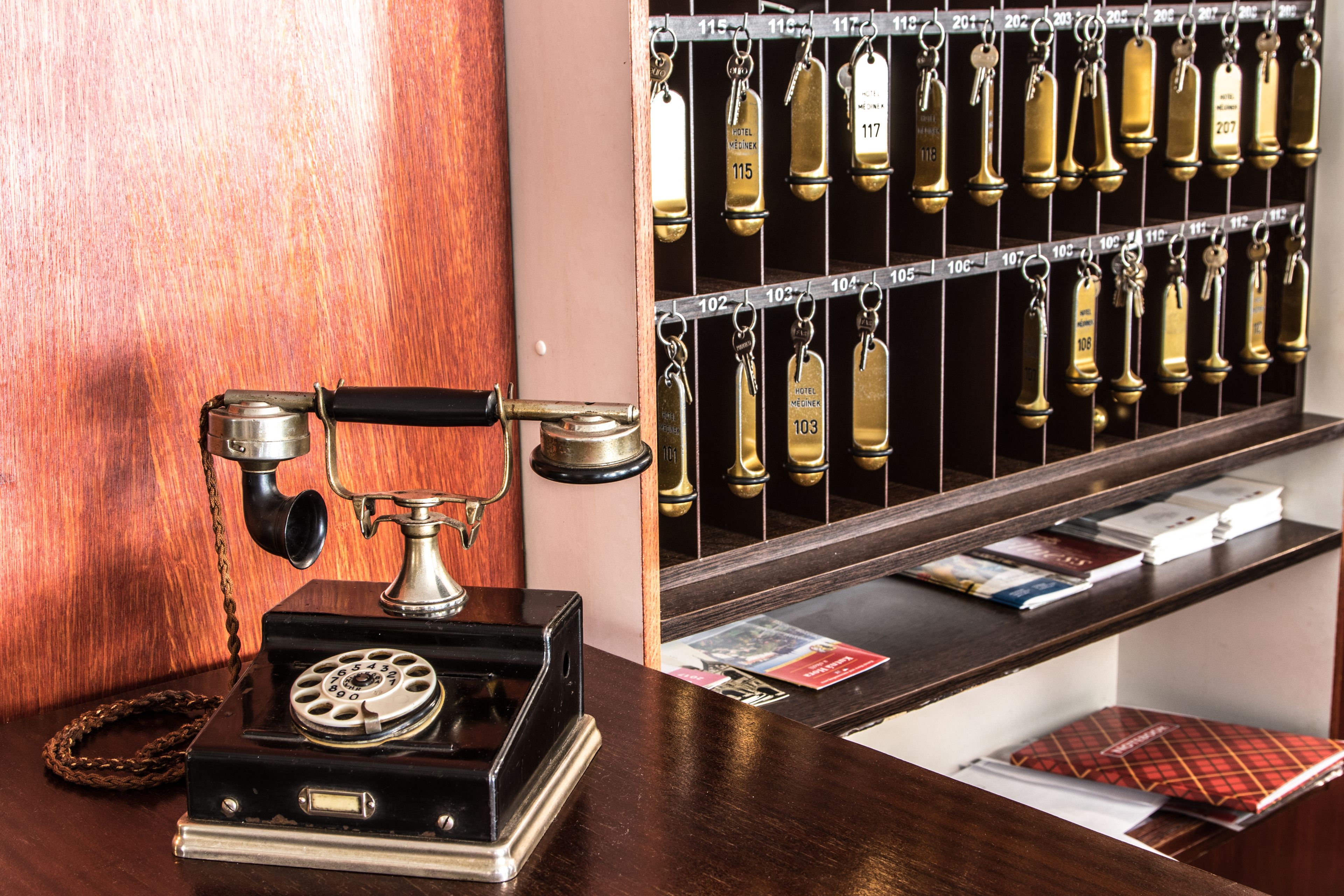 A vintage rotary phone, a metal key rack with numbered keys, and a wooden counter with brochures.