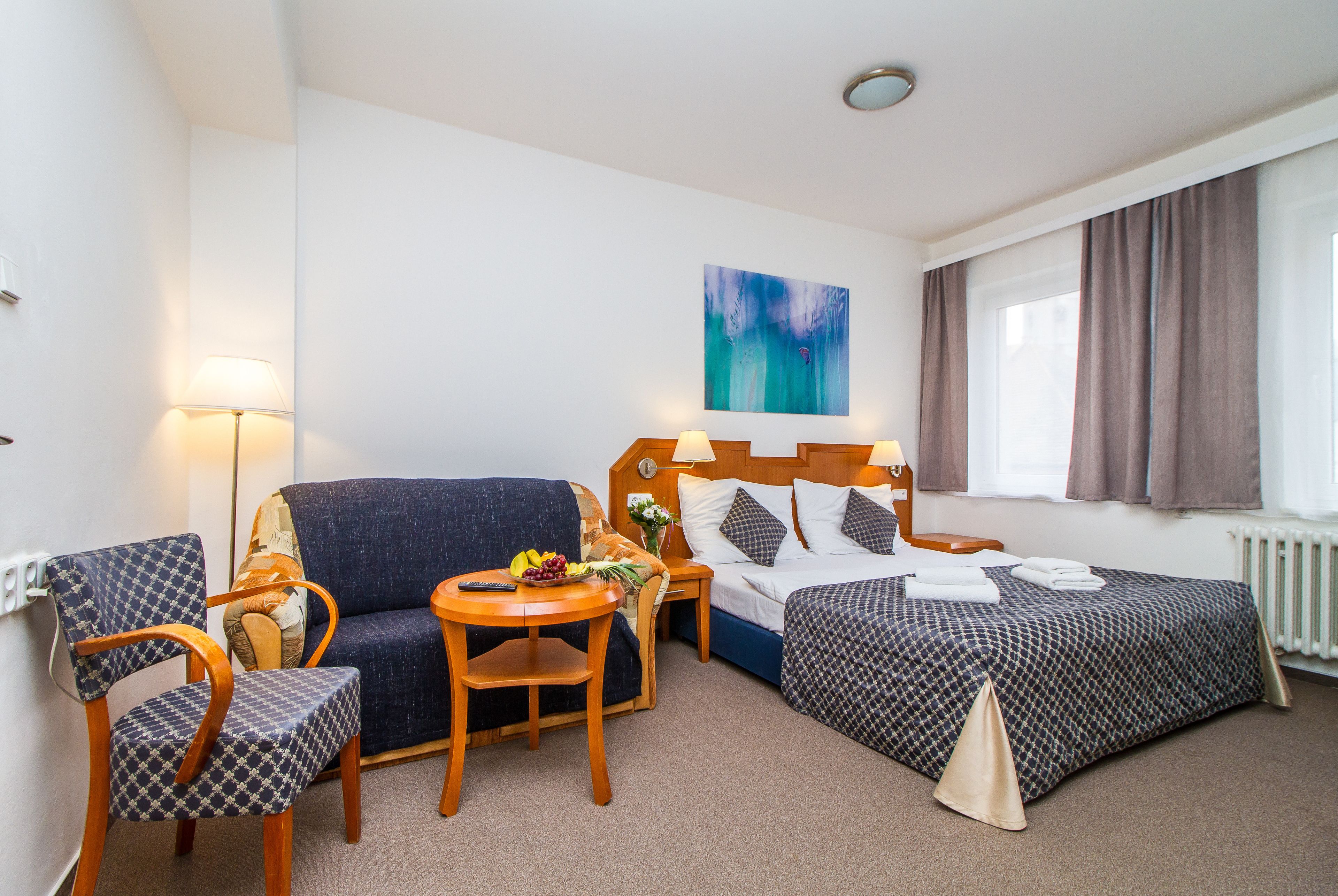 Una habitación de hotel con cama, sofá, sillón, mesita y lámpara.